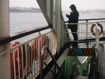 Silhouette of a person on a ferry using a phone with water view.