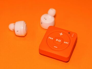 Close-up of wireless earphones and a compact music player on an orange background, showcasing modern audio technology.