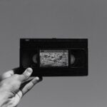 A hand holding a vintage VHS cassette tape against a plain gray background, evoking nostalgia.