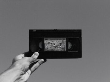 A hand holding a vintage VHS cassette tape against a plain gray background, evoking nostalgia.