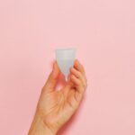 Close-up of a hand holding a silicone menstrual cup on a pink background.