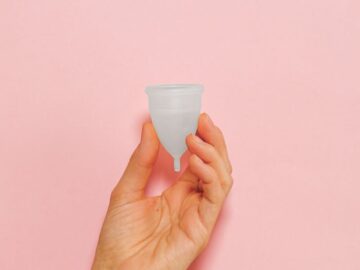 Close-up of a hand holding a silicone menstrual cup on a pink background.
