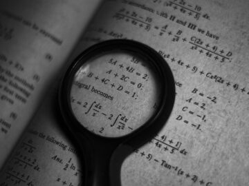 A magnifying glass focuses on mathematics formulas in a book, enhancing study and exploration.