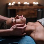 Woman receiving a calming facial massage in a tranquil spa setting with candlelight.