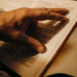 A hand gently touches the pages of an open book with Hebrew text, symbolizing a connection to Jewish traditions.