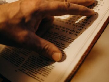 A hand gently touches the pages of an open book with Hebrew text, symbolizing a connection to Jewish traditions.