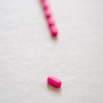 Bright pink pills aligned on a white surface, symbolizing medical treatment or prescription drugs.