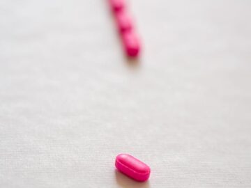 Bright pink pills aligned on a white surface, symbolizing medical treatment or prescription drugs.