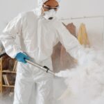A professional in PPE disinfects an indoor space, emphasizing safety and hygiene.