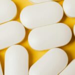 From above closeup of white ellipse shaped medical pills placed on bright yellow surface