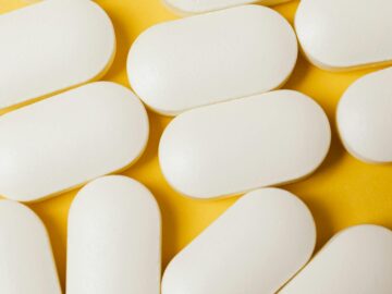 From above closeup of white ellipse shaped medical pills placed on bright yellow surface