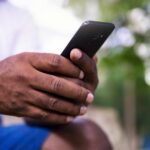 A close-up of a man's hands holding a smartphone in a park setting, showcasing technology use.