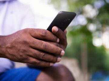 A close-up of a man's hands holding a smartphone in a park setting, showcasing technology use.
