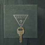 Close-up of a vintage rusty key with the GUESS? logo background, offering an antique charm.