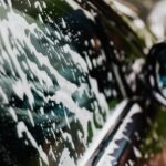 Detailed view of car covered in soapy foam during a wash, highlighting cleanliness.