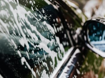 Detailed view of car covered in soapy foam during a wash, highlighting cleanliness.