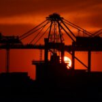 Silhouette of cargo cranes against a vivid sunset at an industrial container port.
