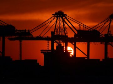Silhouette of cargo cranes against a vivid sunset at an industrial container port.