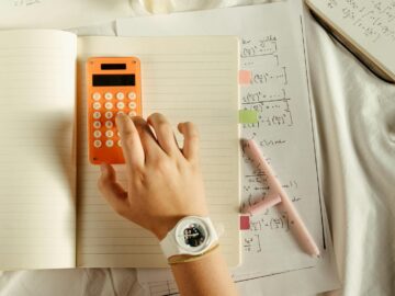 A student calculates math equations using an orange calculator and notebook for study.