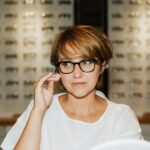 A woman wearing eyeglasses examines her reflection at an optician's store.