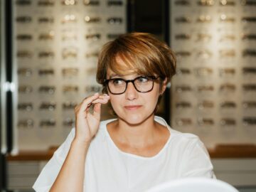 A woman wearing eyeglasses examines her reflection at an optician's store.