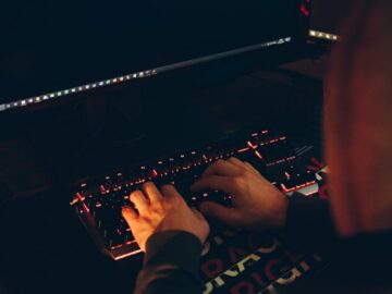 A person in a hoodie typing on a keyboard with a computer screen displaying a curiosity message.