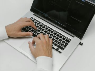 Close-up of hands typing on a laptop with a USB device on a white background. Ideal for tech and cybersecurity themes.