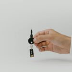 Hand holding keychain with integrated USB flash drive against a plain background.