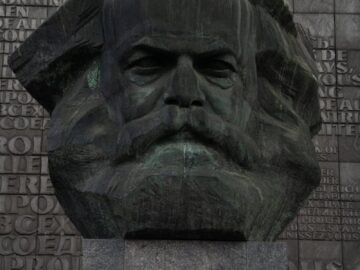 Stone head sculpture of revolutionary placed on high postament against stone wall in city