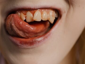 Detailed shot focusing on a mouth with visible fangs and tongue, evoking a vampire aesthetic.