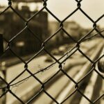 Sepia image of a chain link fence with two locks overlooking a blurred urban street.