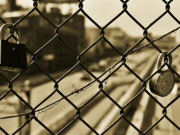 Sepia image of a chain link fence with two locks overlooking a blurred urban street.