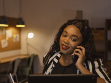 Confident businesswoman multitasking on phone and laptop in a warm office atmosphere.