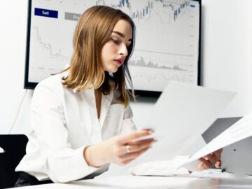 Focused woman analyzing financial reports in a modern office setting with charts and graphs.