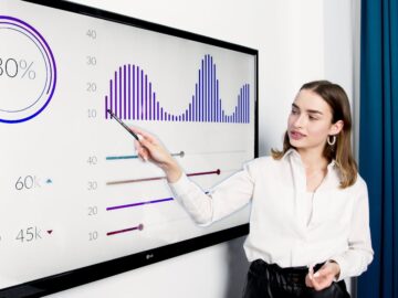 Businesswoman presenting data on a large digital screen in a modern office setting.