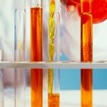 Close-up of a lab technician pouring orange liquid into test tubes in a laboratory setting.