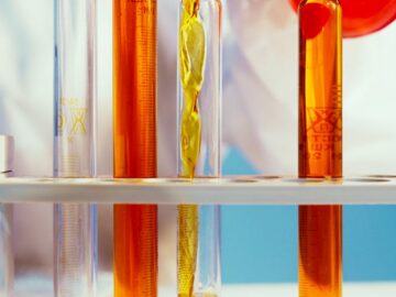 Close-up of a lab technician pouring orange liquid into test tubes in a laboratory setting.