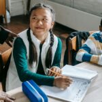 Crop black teacher talking with smart multiethnic boy and girl siting at desk with notepads