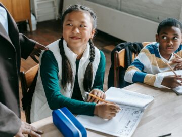Crop black teacher talking with smart multiethnic boy and girl siting at desk with notepads