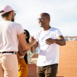 Happy smiling multiethnic male friends greeting each other and shaking hands while gathering on rooftop in urban city