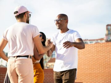 Happy smiling multiethnic male friends greeting each other and shaking hands while gathering on rooftop in urban city