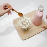 Close-up of hands reaching for a dessert topped with whipped cream beside a bottle of pink milk.