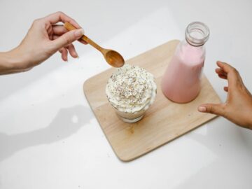 Close-up of hands reaching for a dessert topped with whipped cream beside a bottle of pink milk.