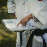 Close-up of martial artist holding and pointing at a reference book outdoors.