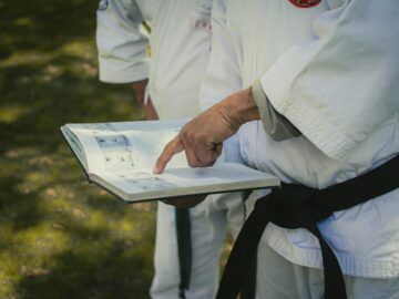 Close-up of martial artist holding and pointing at a reference book outdoors.