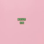 Inspirational text "Move On" spelled with green tiles on a pink background. Minimalist design, perfect for motivation.