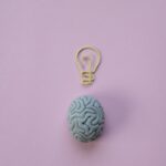 Brain-shaped eraser with a light bulb paperclip on a pastel pink background. Ideal for education and creativity themes.
