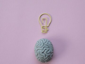 Brain-shaped eraser with a light bulb paperclip on a pastel pink background. Ideal for education and creativity themes.