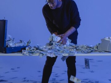 A man interacts with scattered dollar bills in a blue-lit modern setting.