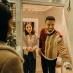 A couple greeting a guest at their doorway, capturing the warmth of a home during the holiday season.